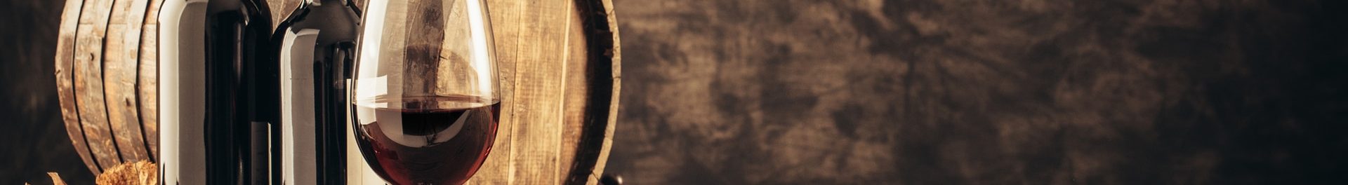 Wine glass, wooden barrel and collection of excellent red wine bottles in the cellar: traditional winemaking and wine tasting concept