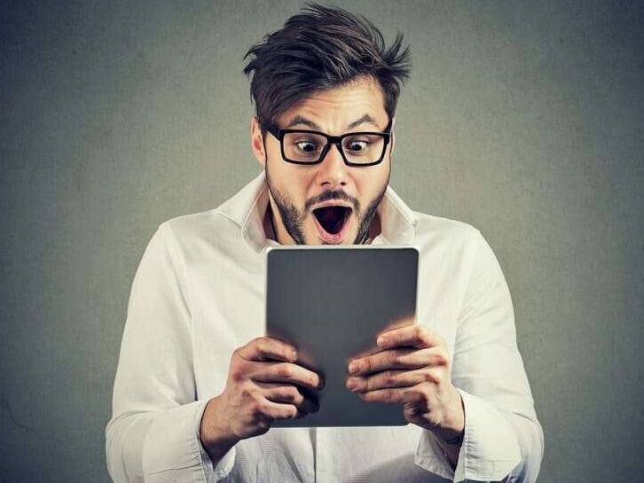 LANDINGPAGE_2025 8 Young man in eyeglasses watching tablet with shock having bad news and posing on gray background